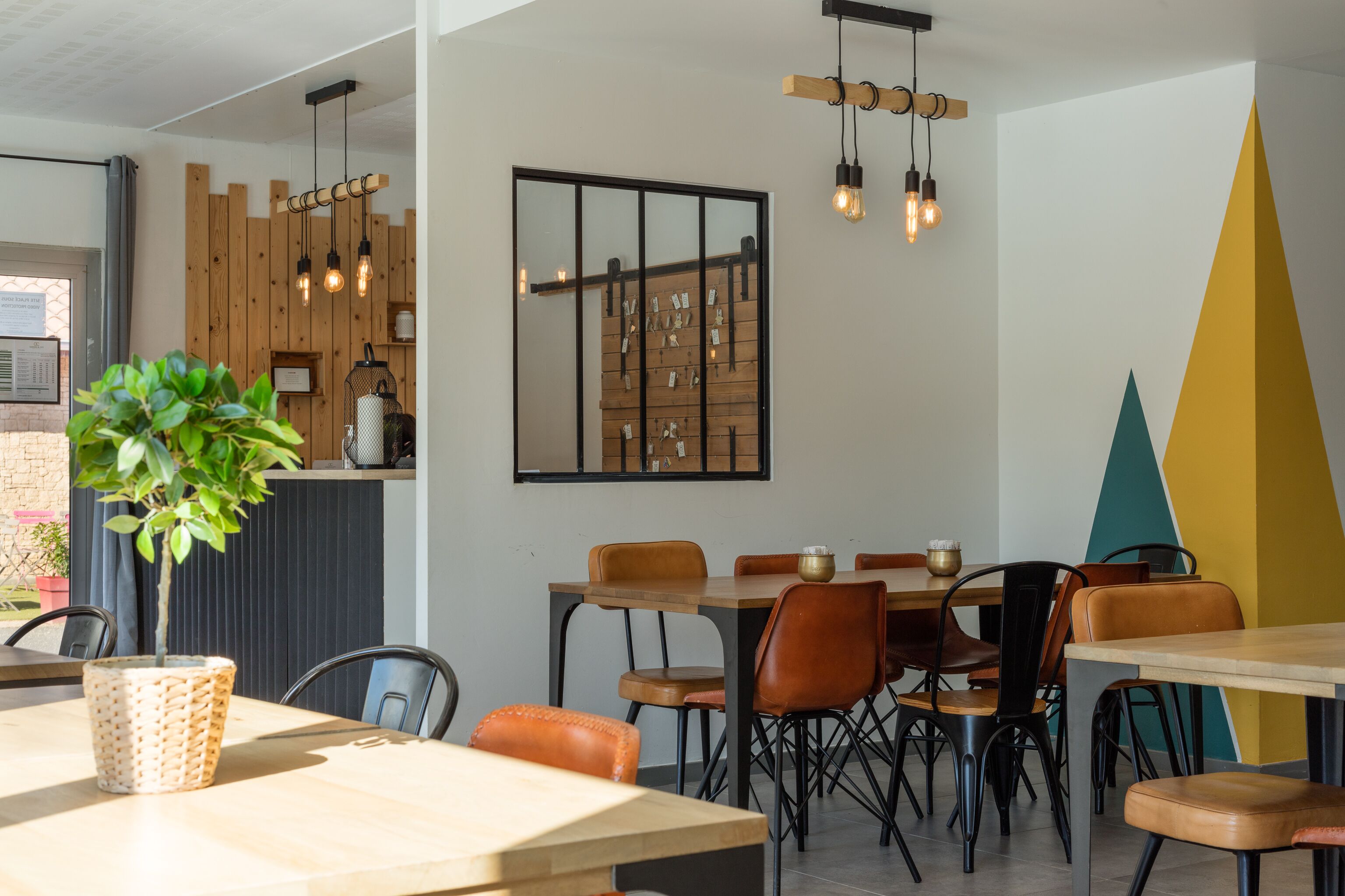 Een moderne eetruimte met houten tafels en stoelen, een potplant en een wandlamp.