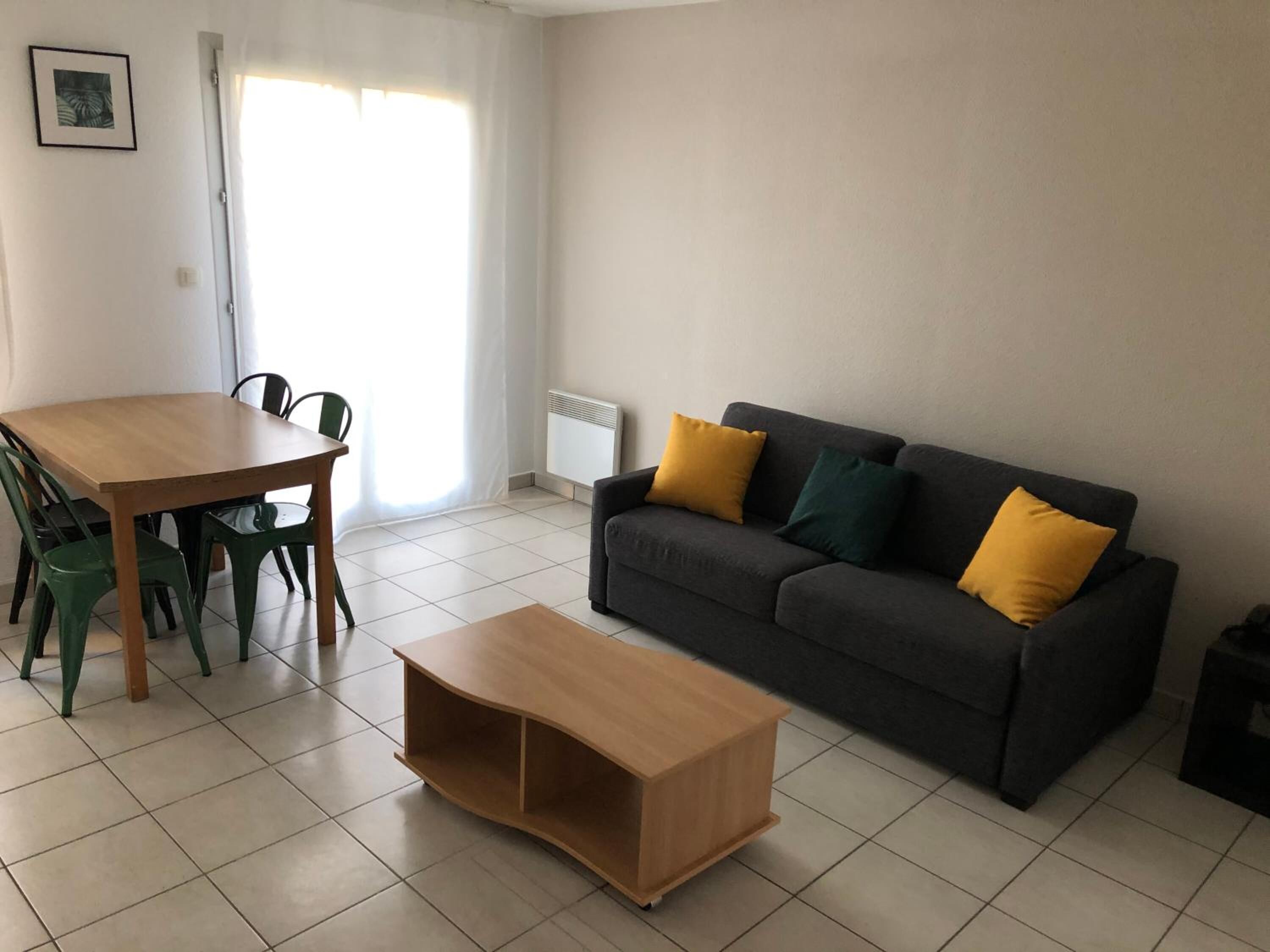 A living room with a wooden table, green chairs, a dark grey sofa with yellow and green cushions, and a wooden coffee table.