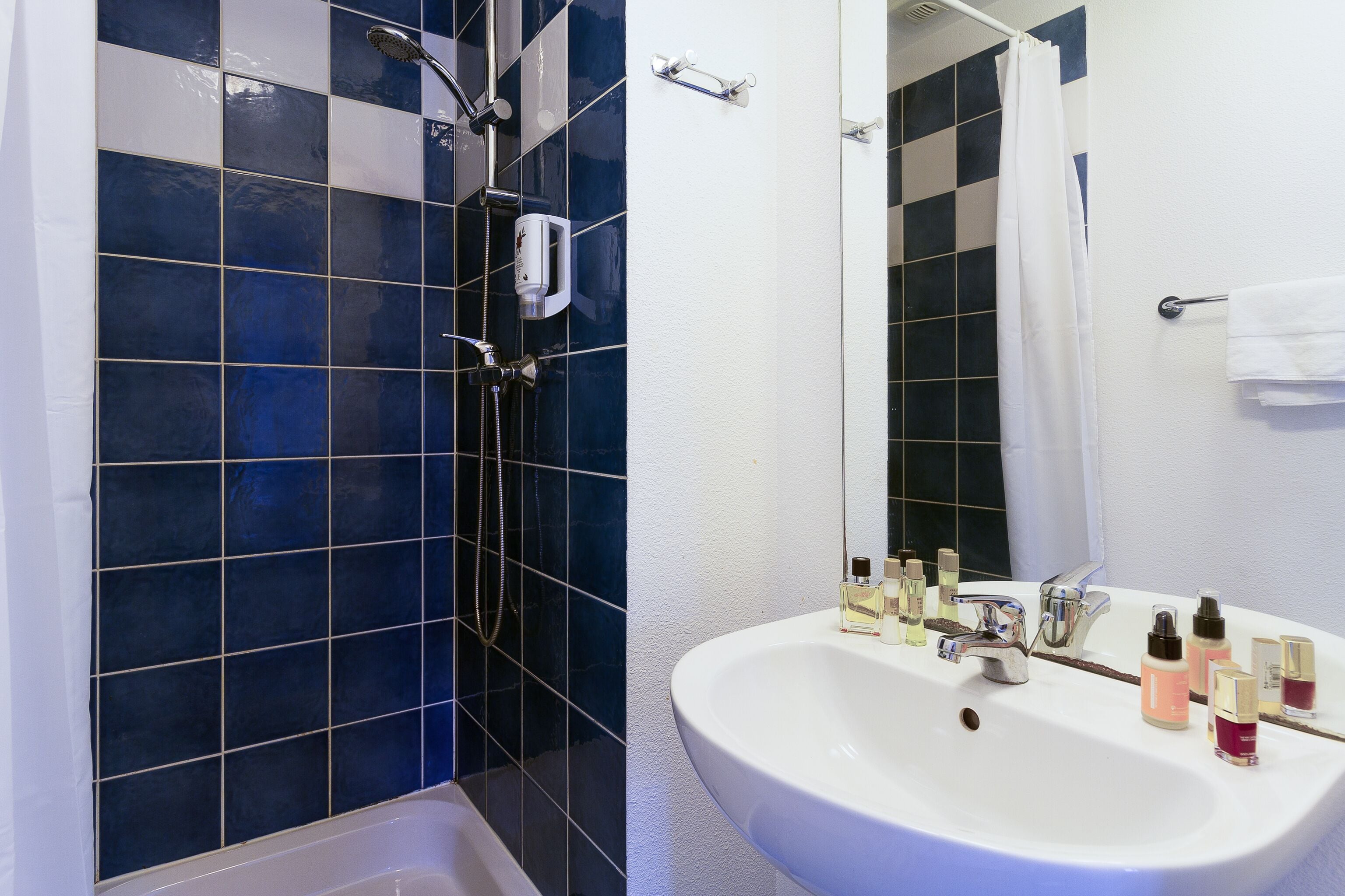 A bathroom with a white sink, blue and white tiled walls, a shower area, and a mirror.