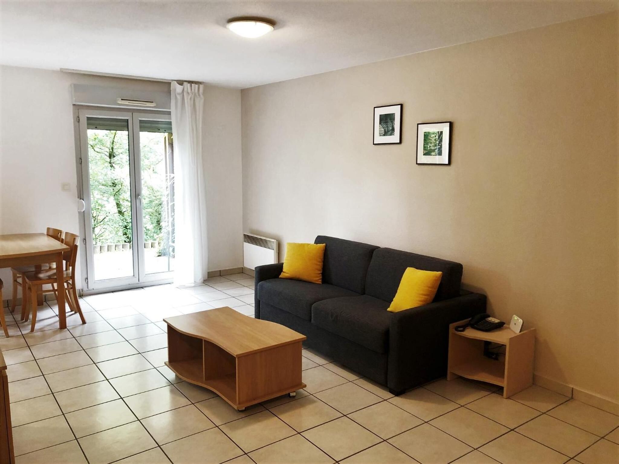 A living room with a sofa, a coffee table, a dining table, and chairs. There is a sliding glass door leading to a balcony.