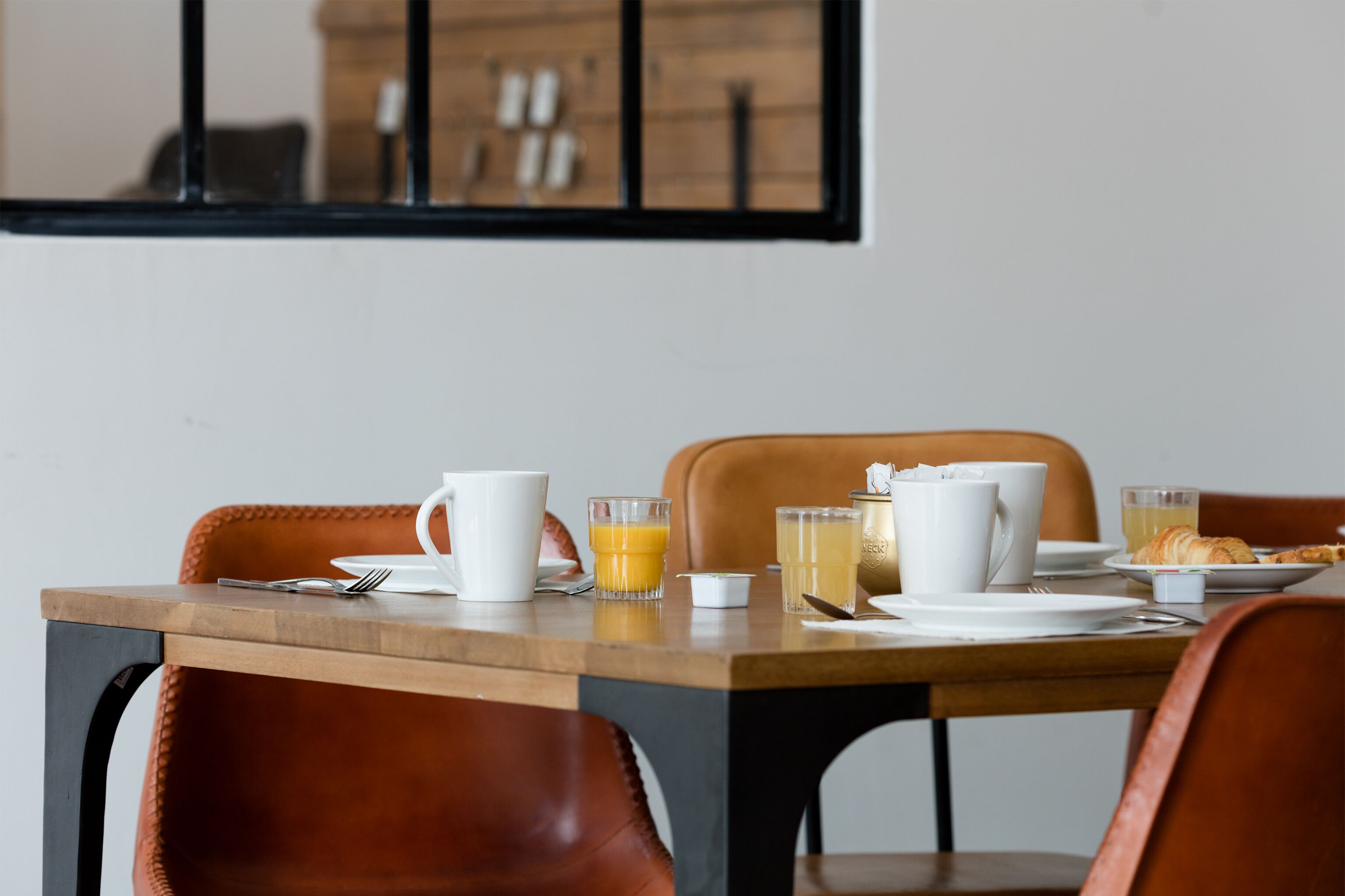 A breakfast table set with plates, cups, and glasses, including orange juice and tea, in a modern room with leather chairs and a wooden table.