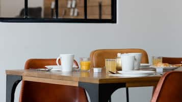 A breakfast table set with plates, cups, and glasses, including orange juice and tea, in a modern room with leather chairs and a wooden table.