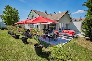 A patio area with outdoor seating, potted plants, and a building with a green logo. - Campanile Evry Ouest - Corbeil Essonnes (Corbeil-Essonnes)