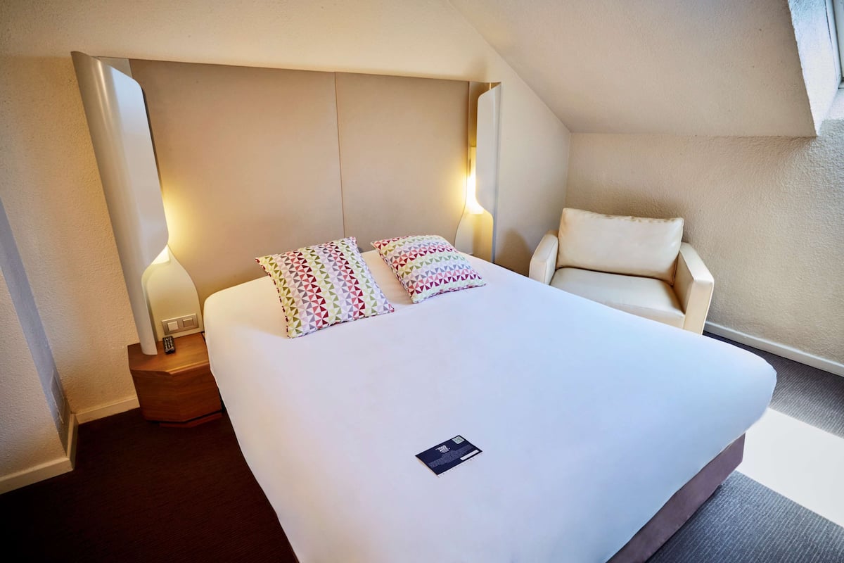 A hotel room with a large bed, two bedside lamps, a chair, and a nightstand.