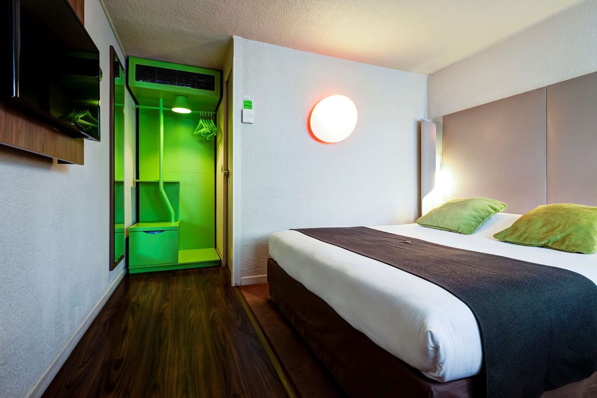 A hotel room with a bed, green lighting, a wall-mounted TV, and a circular light fixture.