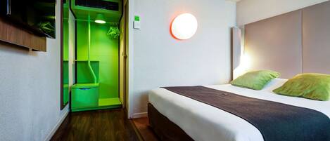A hotel room with a bed, green lighting, a wall-mounted TV, and a circular light fixture.