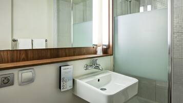 A modern bathroom with a white sink, a mirror with a wooden frame, a shower area, and a soap dispenser.