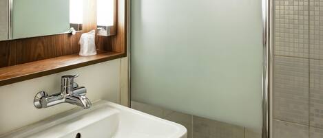 Un baño con lavamanos blanco, un espejo con marco de madera y cabina de ducha con mampara de vidrio.