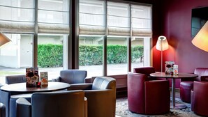A modern lounge area with comfortable seating, large windows with blinds, and a flat-screen TV mounted on the wall. - Campanile Evry Ouest - Corbeil Essonnes (Corbeil-Essonnes)