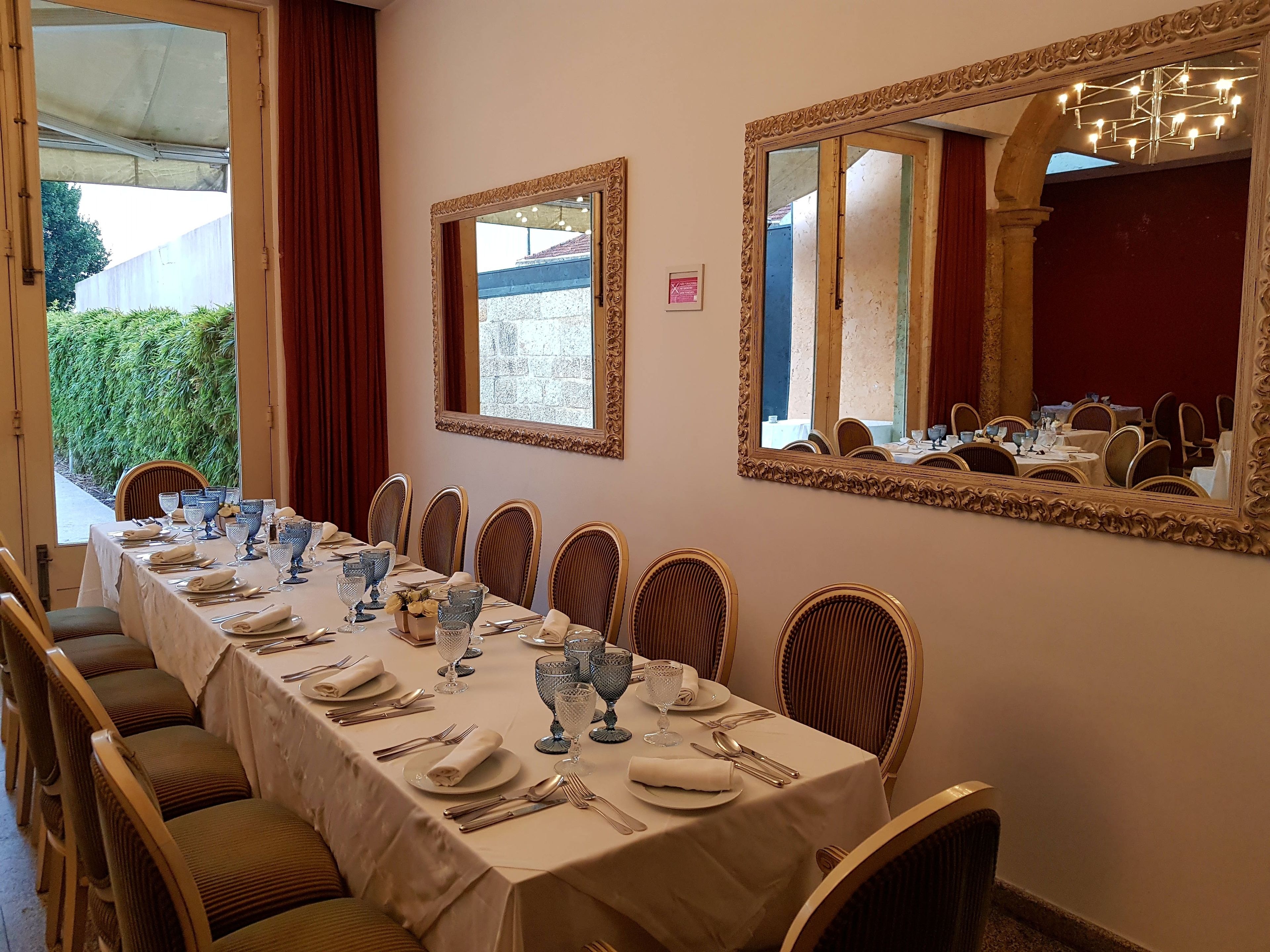 Een eetzaal met een lange tafel, gedekt voor een maaltijd, omringd door stoelen en twee grote spiegels aan de wanden.