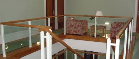 Amplia sala de estar con escalera de madera, sofá floral y barandilla de vidrio.