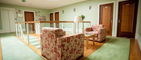 Un vestíbulo amplio con techo alto, una escalera y una zona de estar con mobiliario estampado de flores.