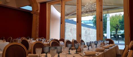 A dining area with a long table set for a meal, large windows, and a chandelier.