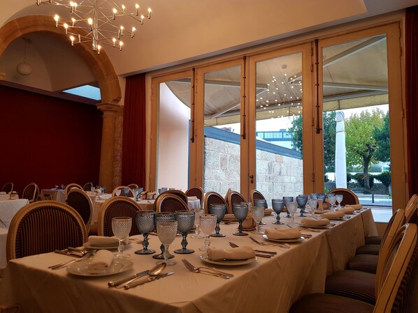 A dining area with a long table set for a meal, large windows, and a chandelier.