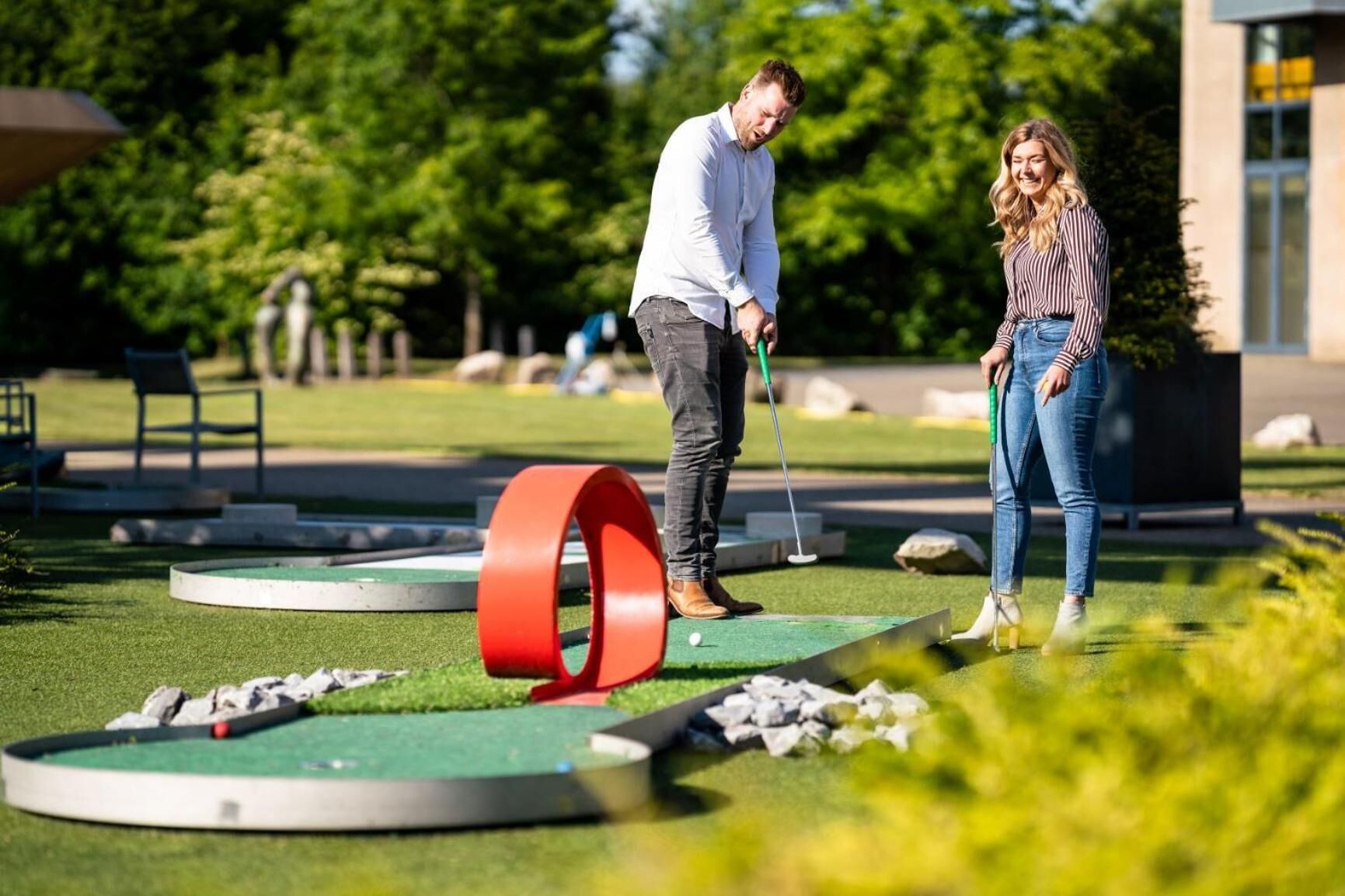 A miniature golf course with a putting green, a red circular obstacle, and a golf ball.