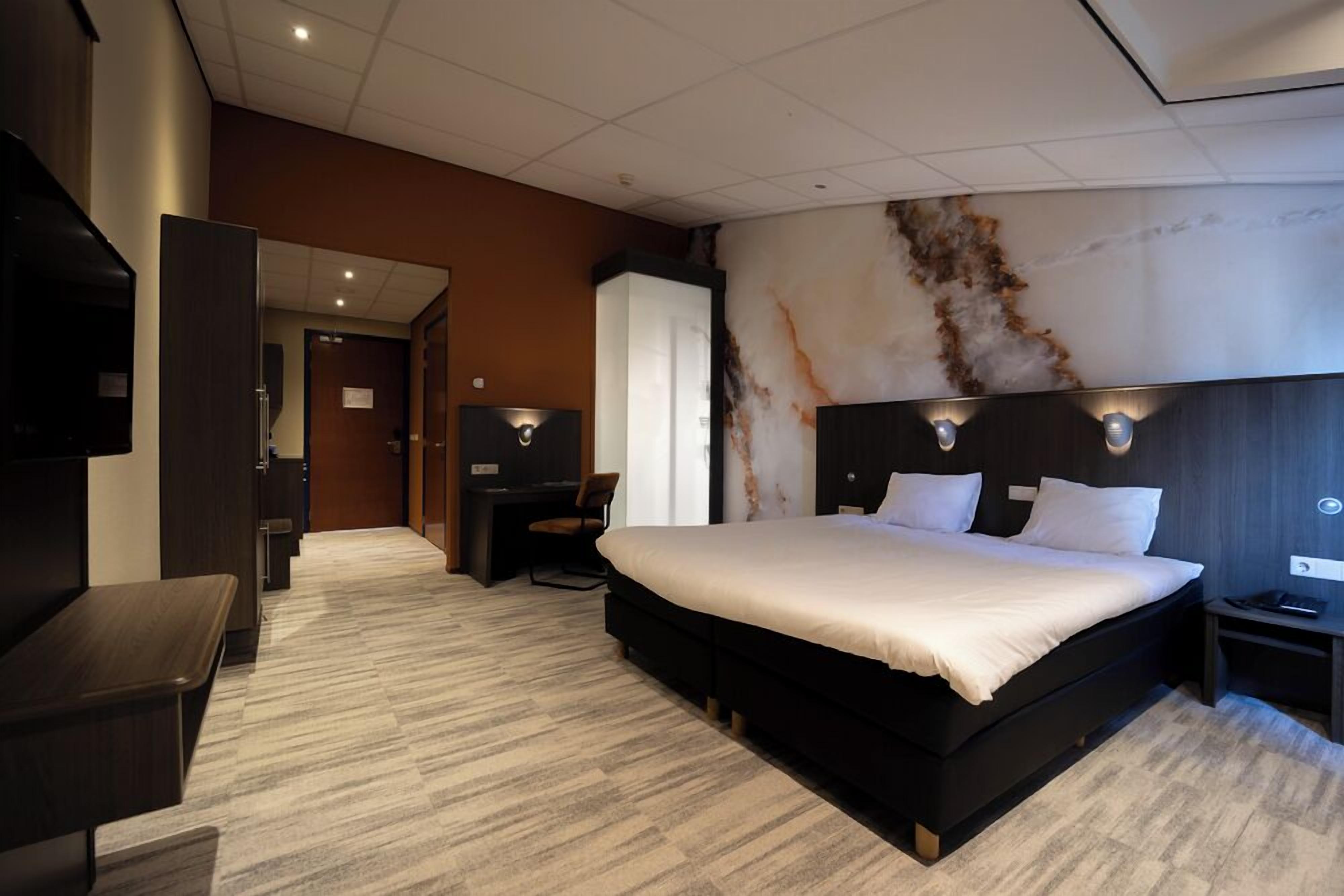 A modern hotel room with a large bed, a desk, a chair, and a TV.