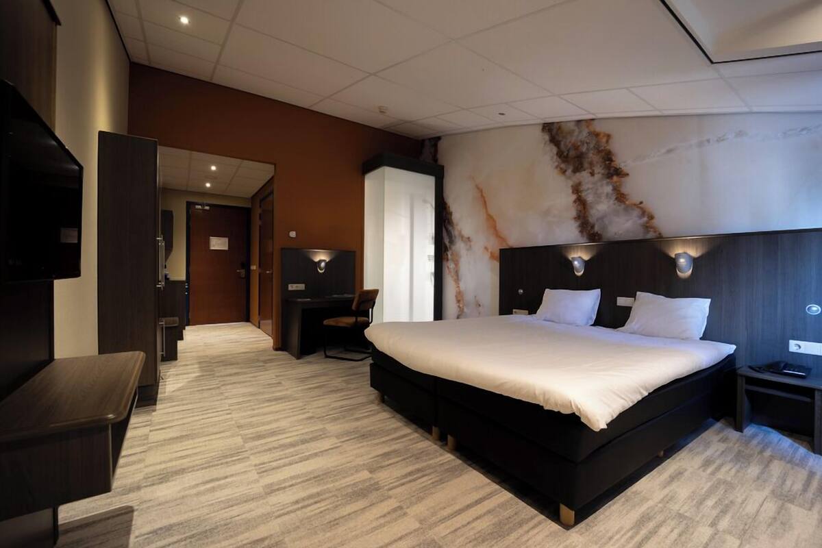A modern hotel room with a large bed, a desk, a chair, and a TV.