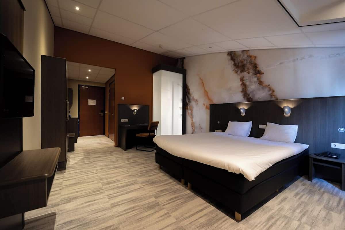 A modern hotel room with a large bed, a desk, a chair, and a TV.