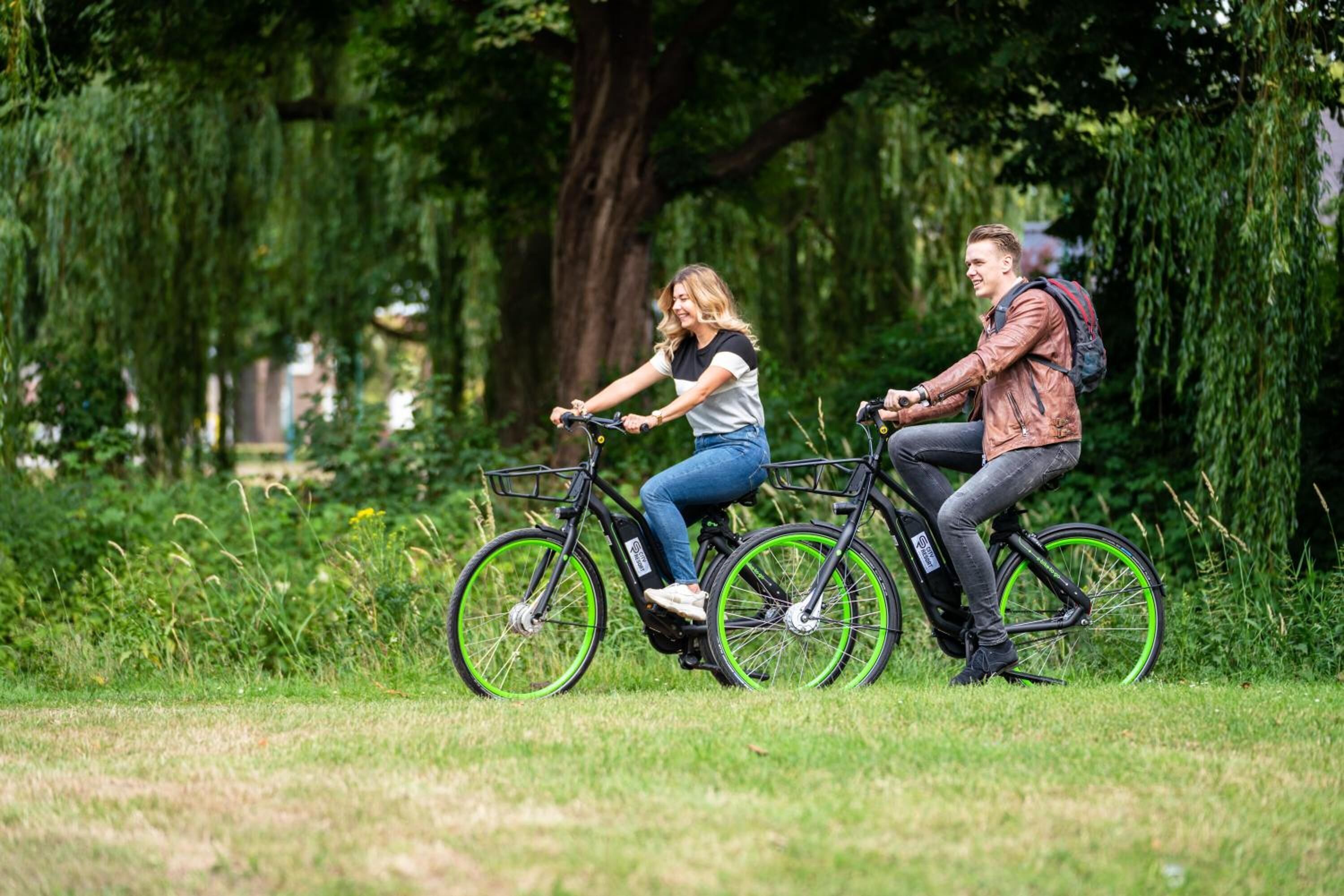 Two people riding bicycles in a park with trees and grass.