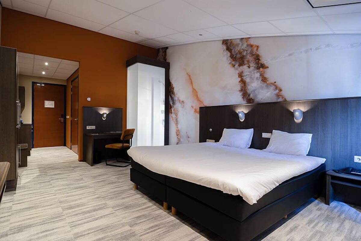 A modern hotel room with a large bed, a desk with a chair, a television, and a marble wall.