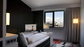 Habitación de hotel moderna con una cama grande, un escritorio, una silla, un televisor y una ventana con vistas a la ciudad.