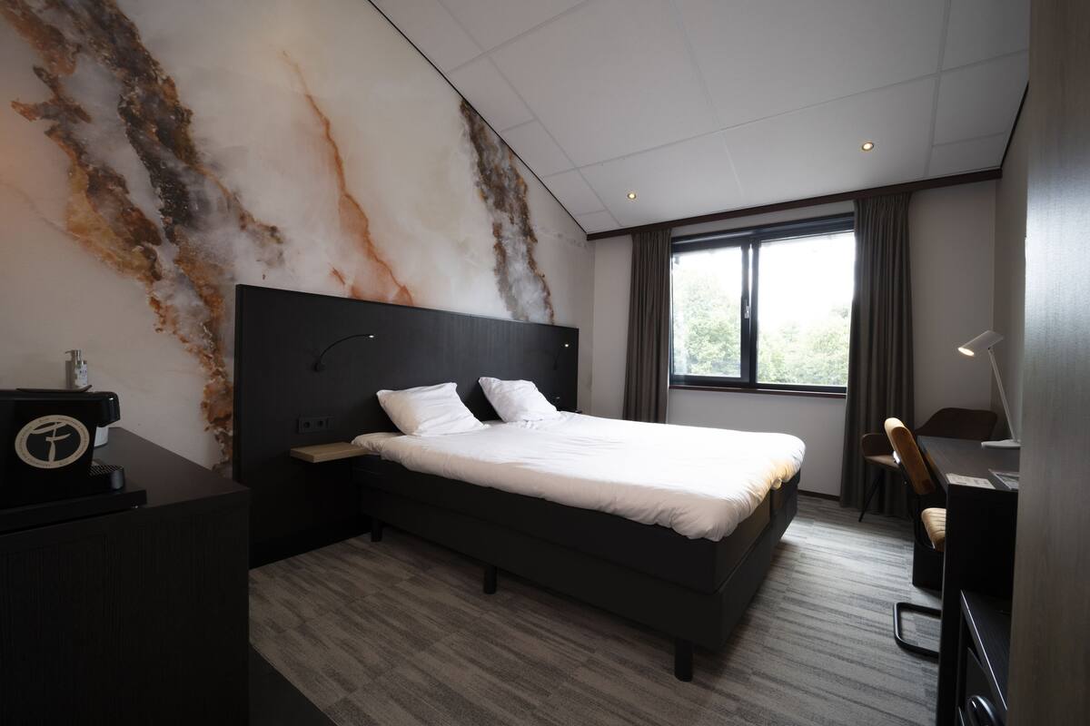 A modern hotel room with a large bed, a desk, and a chair.