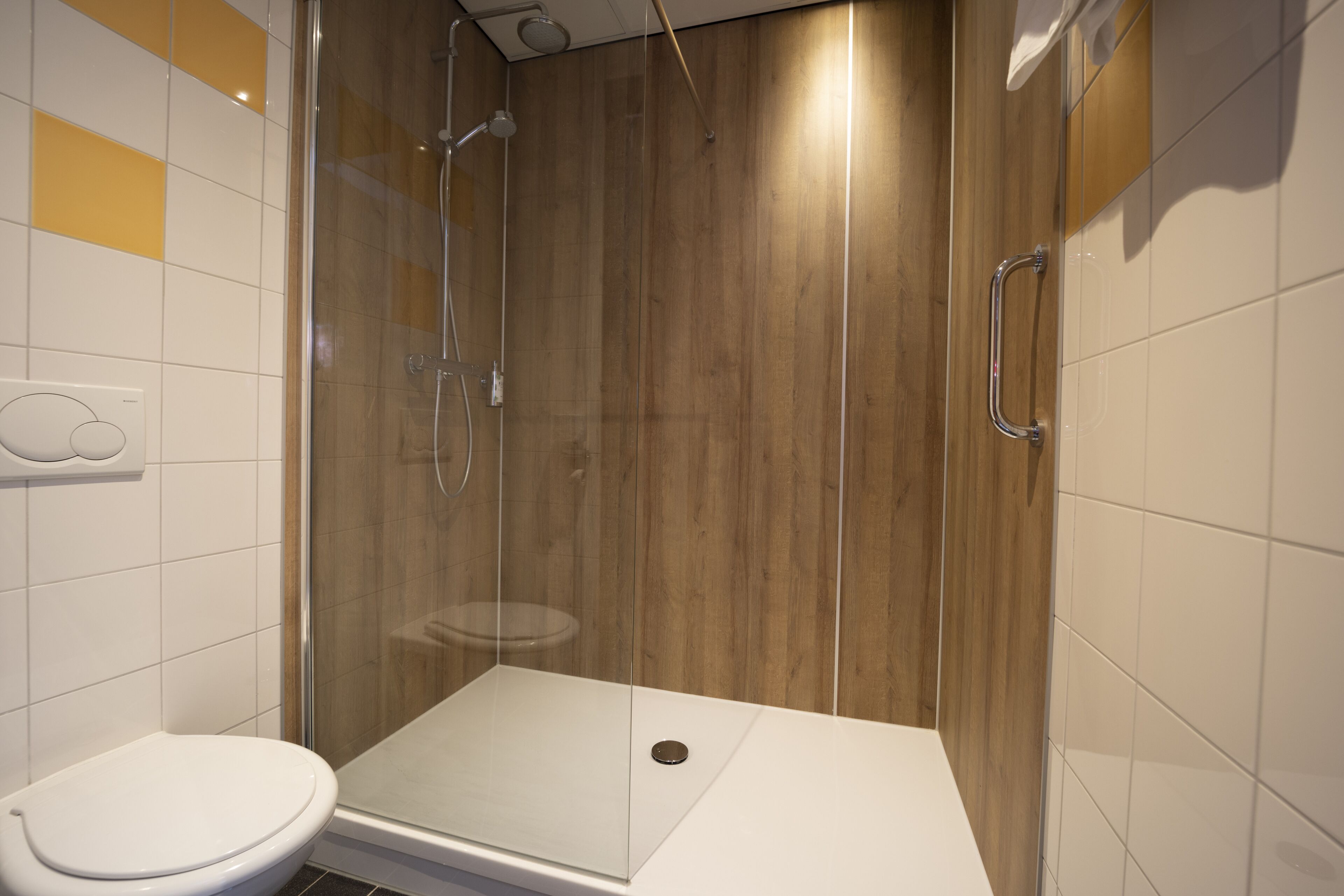A modern bathroom with a glass-enclosed shower, a white toilet, and wooden paneling on the walls.