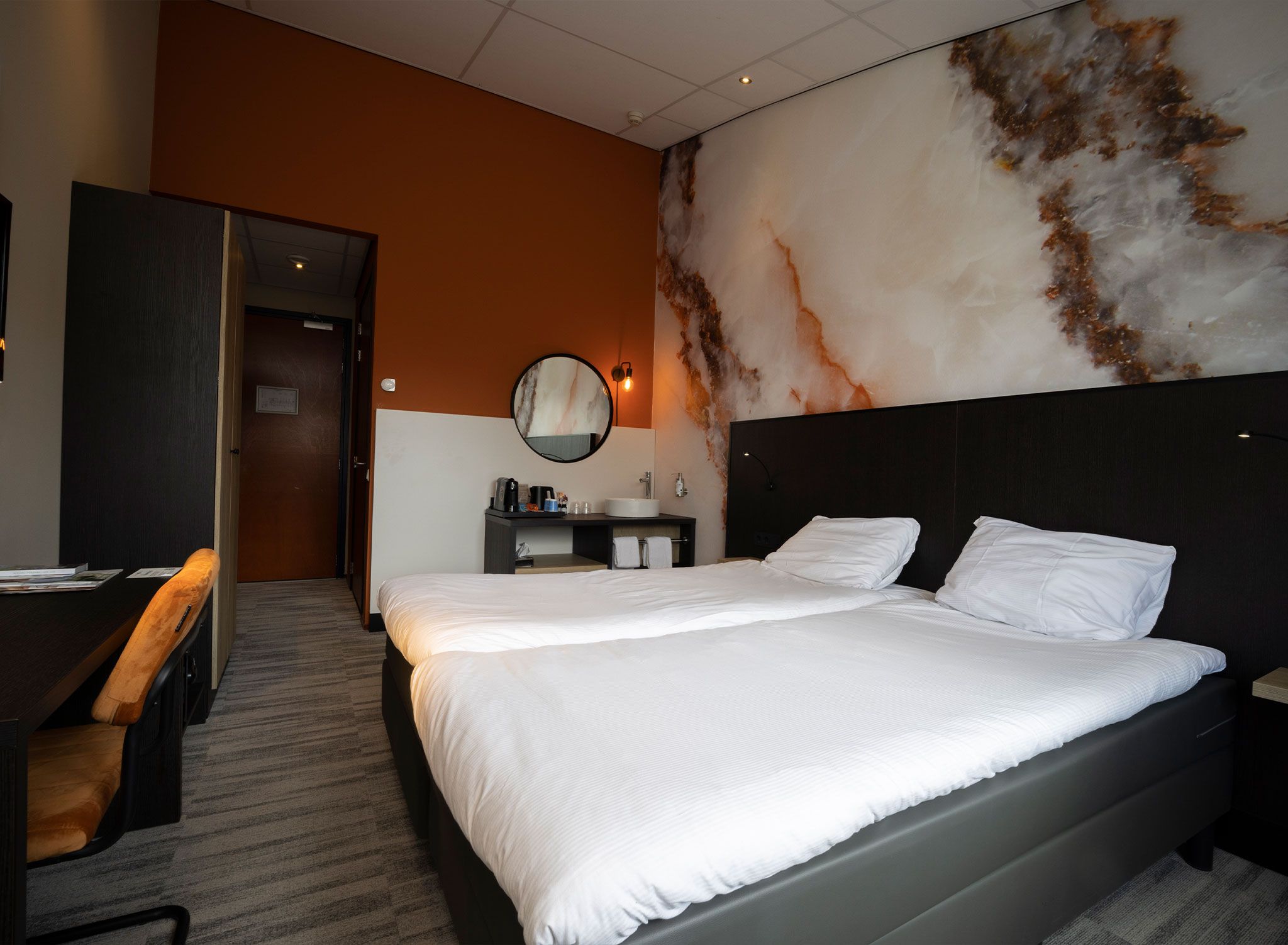 Een hotelkamer met een groot bed, een bureau en een badkamer met een marmeren wand.