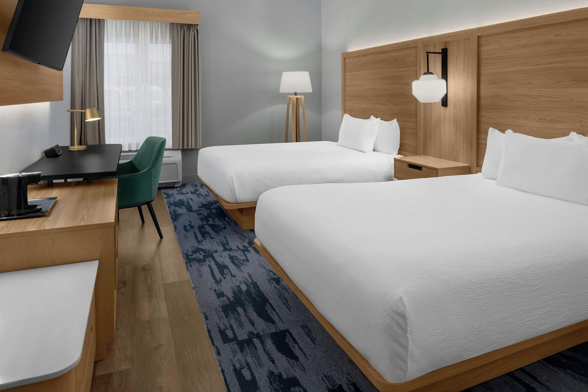 Une chambre d’hôtel avec deux lits, un bureau avec une chaise, une télévision, une lampe et une fenêtre avec des rideaux.
