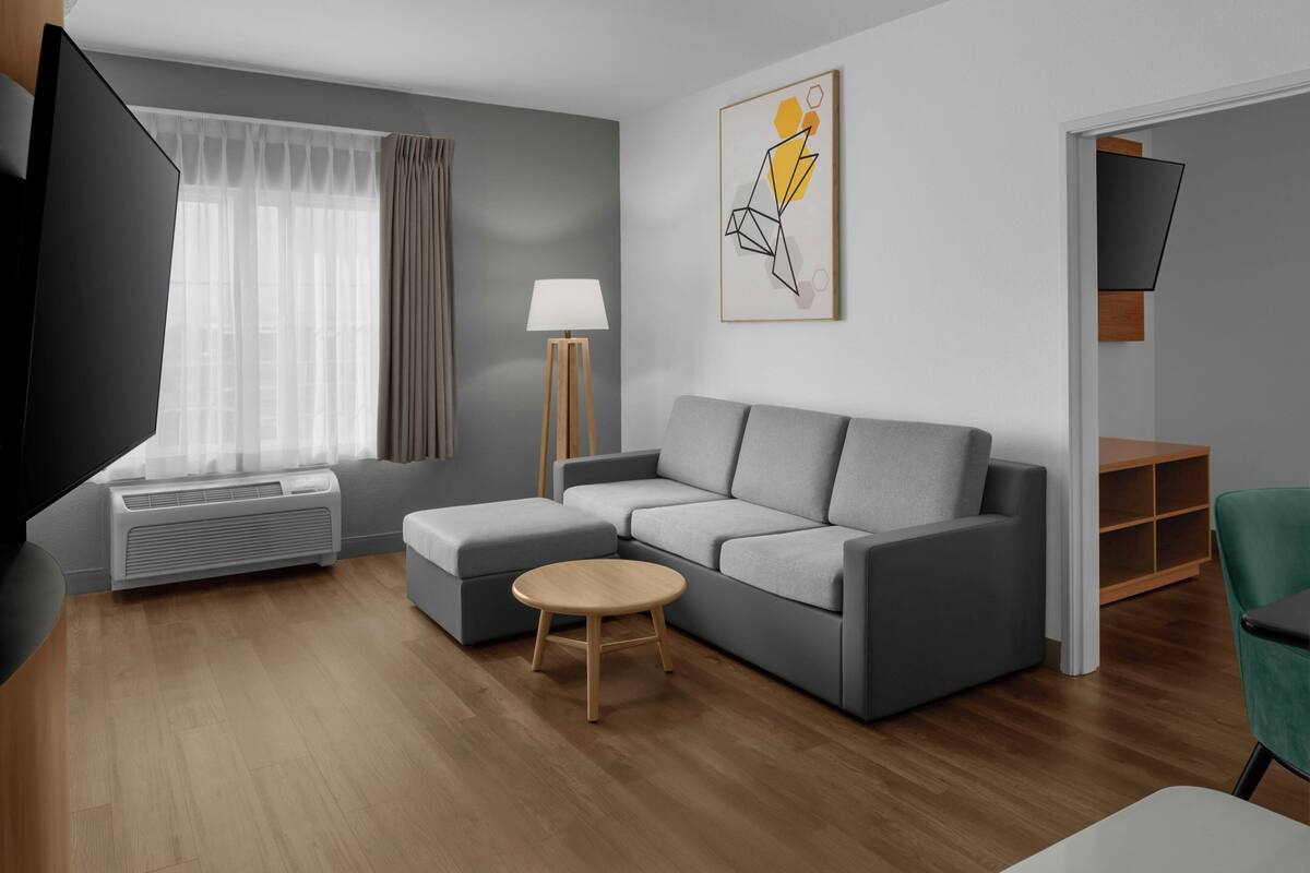 Un soggiorno moderno con un divano grigio, un tavolino rotondo in legno, una lampada da terra e un quadro appeso al muro.