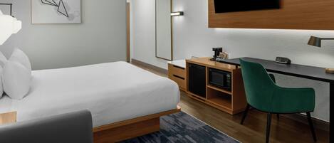 Habitación de hotel moderna con cama, escritorio, silla verde, televisor de pantalla plana y una obra de arte en la pared.