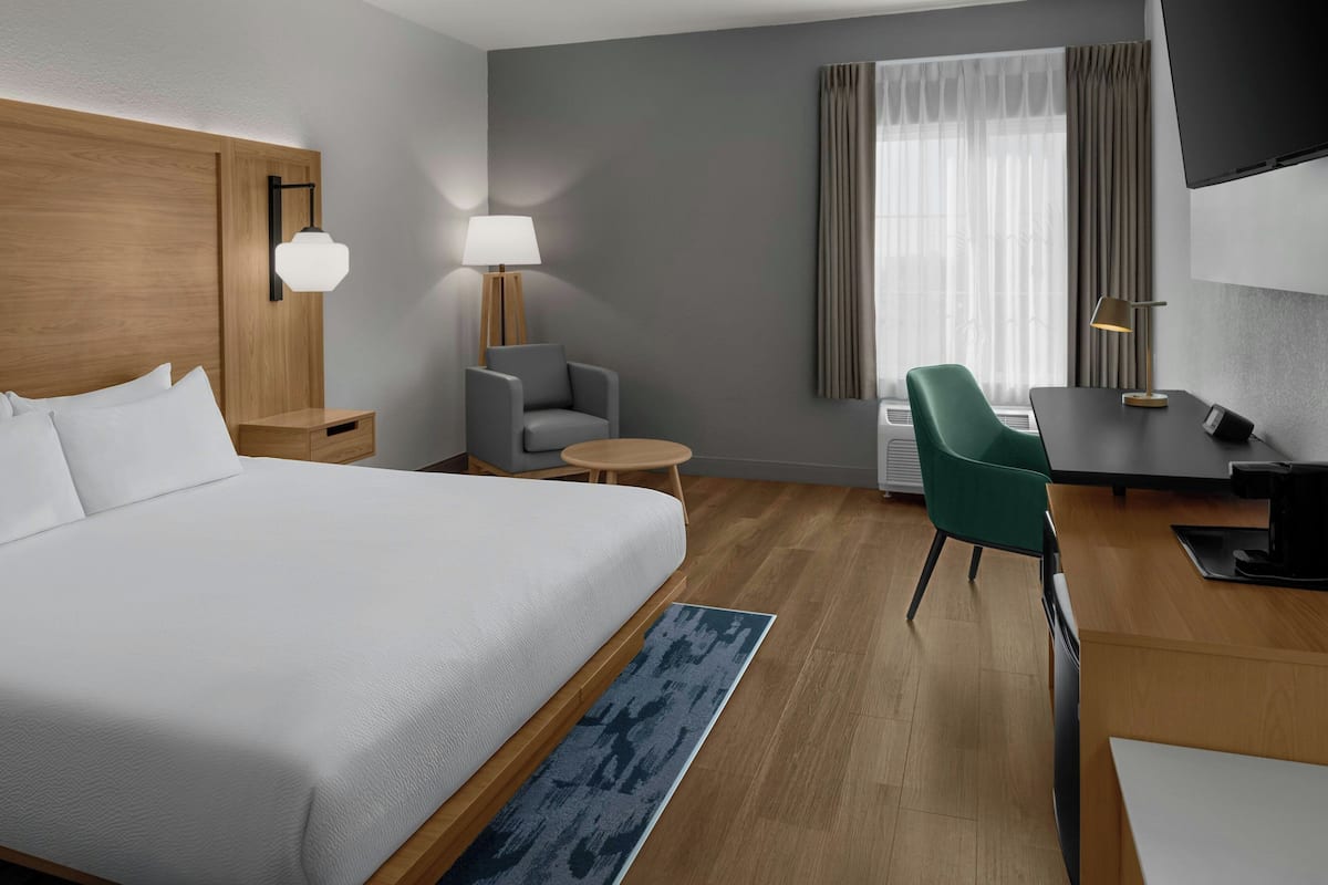 Une chambre d’hôtel avec un lit, un bureau, une chaise, une lampe et un téléviseur.