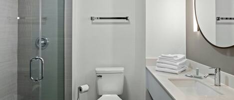 A modern bathroom with a glass shower enclosure, a toilet, a sink with a mirror, and neatly stacked towels.