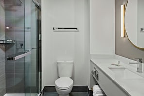 Un baño moderno con cabina de ducha de vidrio, inodoro y lavamanos blancos, y un espejo.