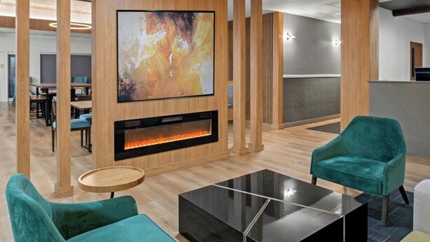 A modern lounge area with teal chairs, a black coffee table, a fireplace, and a large abstract painting on the wall. - Fairfield Inn and Suites by Marriott Sacramento Elk Grove (Elk Grove)