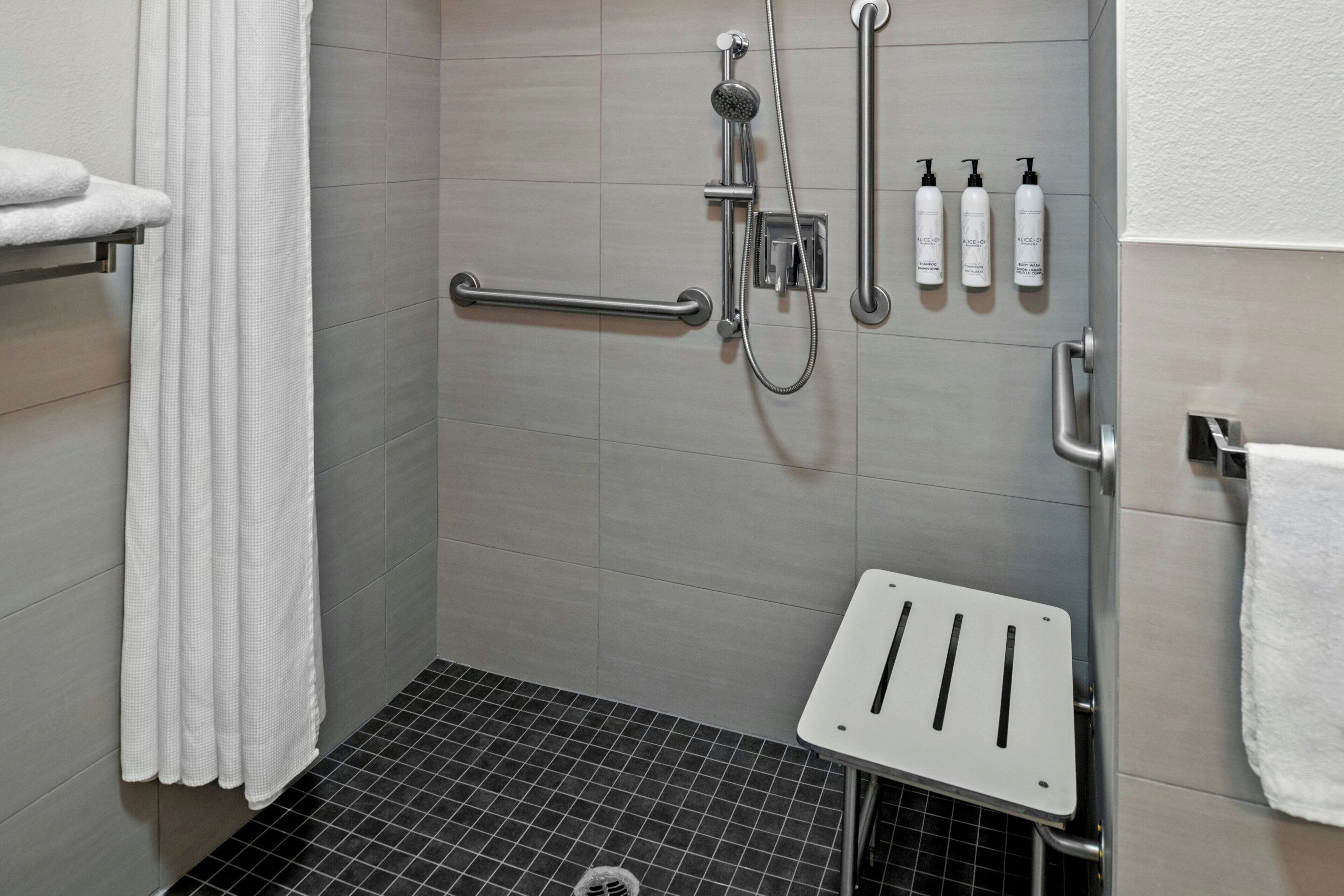A shower area with a handheld showerhead, a handheld showerhead, a towel rack, and a shelf with toiletries.