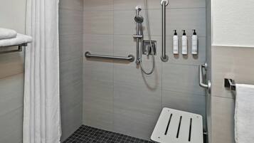 A shower area with a handheld showerhead, a handheld showerhead, a towel rack, and a shelf with toiletries.
