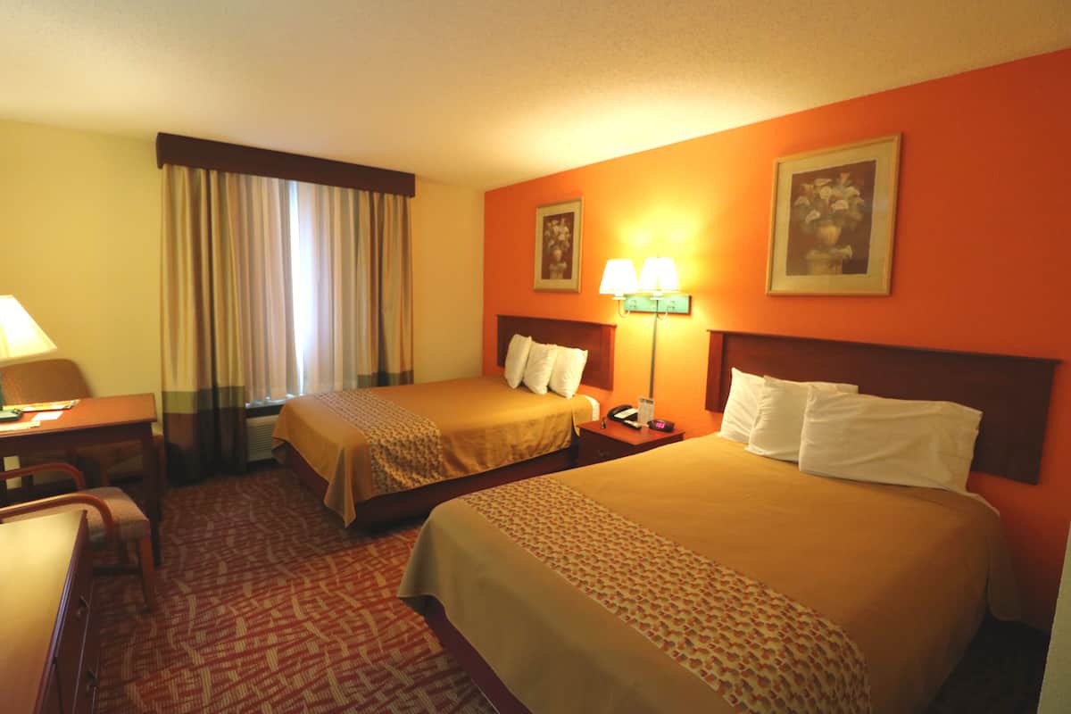 A hotel room with two beds, a desk, a chair, a lamp, and a window with curtains.