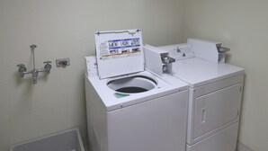 A compact, white laundry room with a front-loading washing machine, a built-in dryer, and a wall-mounted sink. - Jefferson Inn Dandridge (Dandridge)