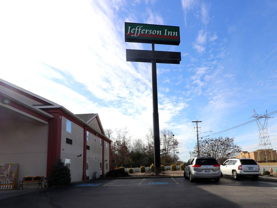 A motel named Jefferson Inn with a parking lot, a small outdoor seating area, and a clear sky.