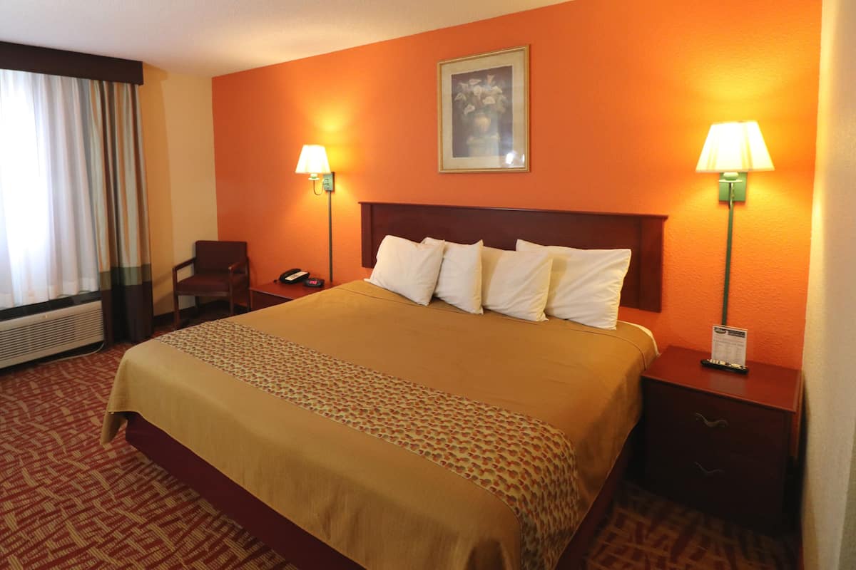 A hotel room with a large bed, two bedside lamps, a chair, a desk with a phone, and a window with curtains.