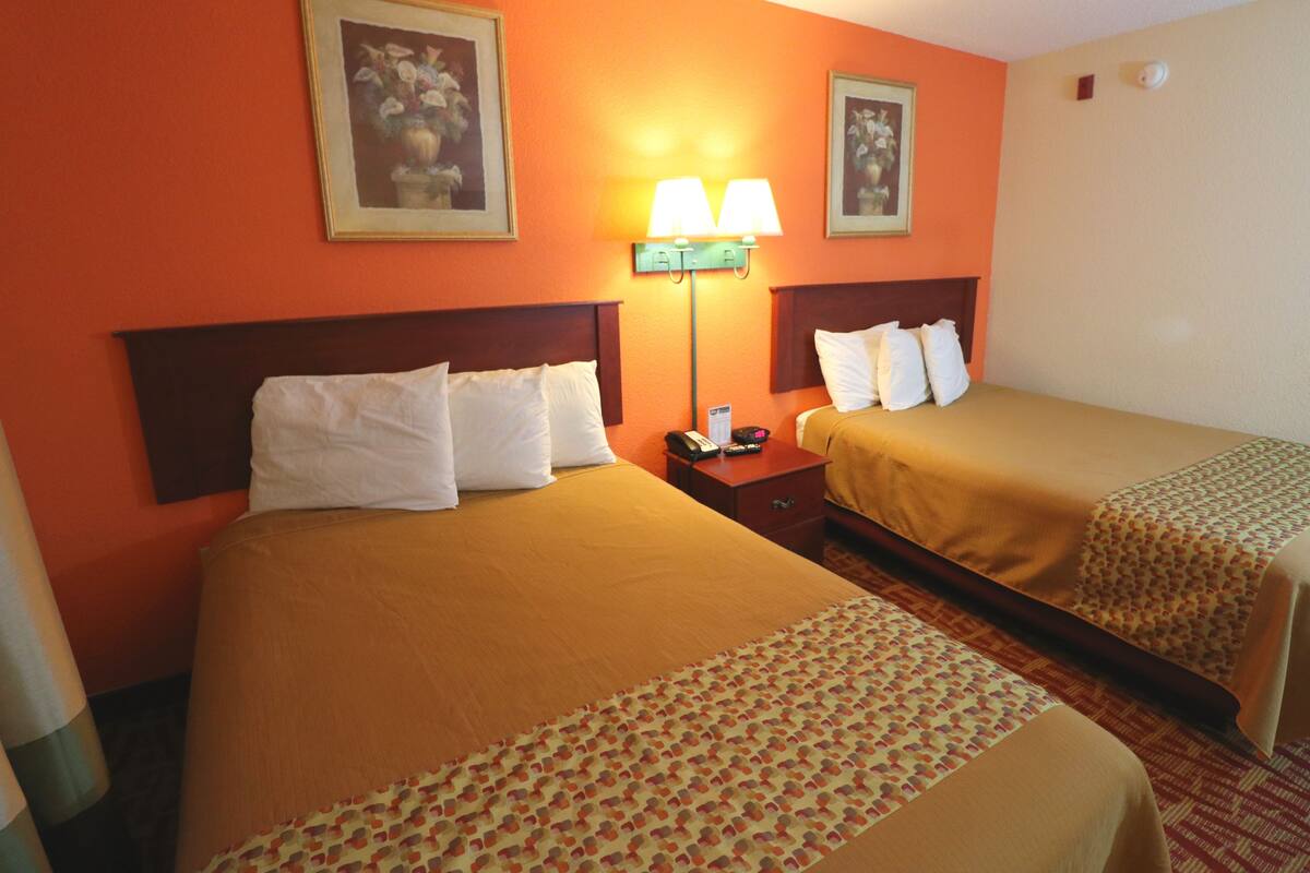A hotel room with two beds, a nightstand, a lamp, and two framed pictures on the wall.