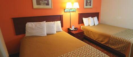 Quarto de hotel com duas camas, uma mesa de cabeceira, uma luminária e duas molduras na parede.