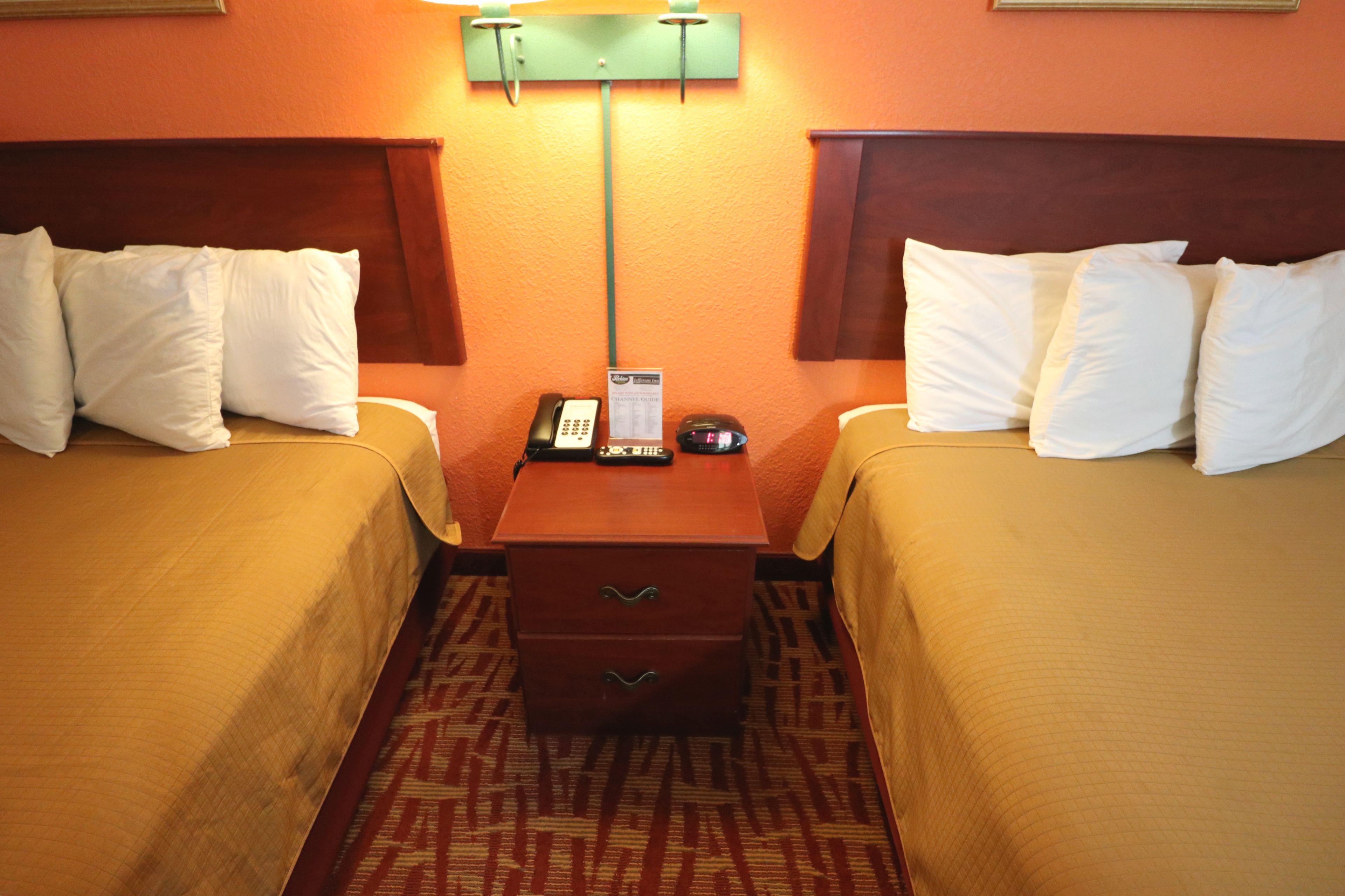 Una habitación de hotel con dos camas, una mesita de noche, un teléfono y una lámpara.