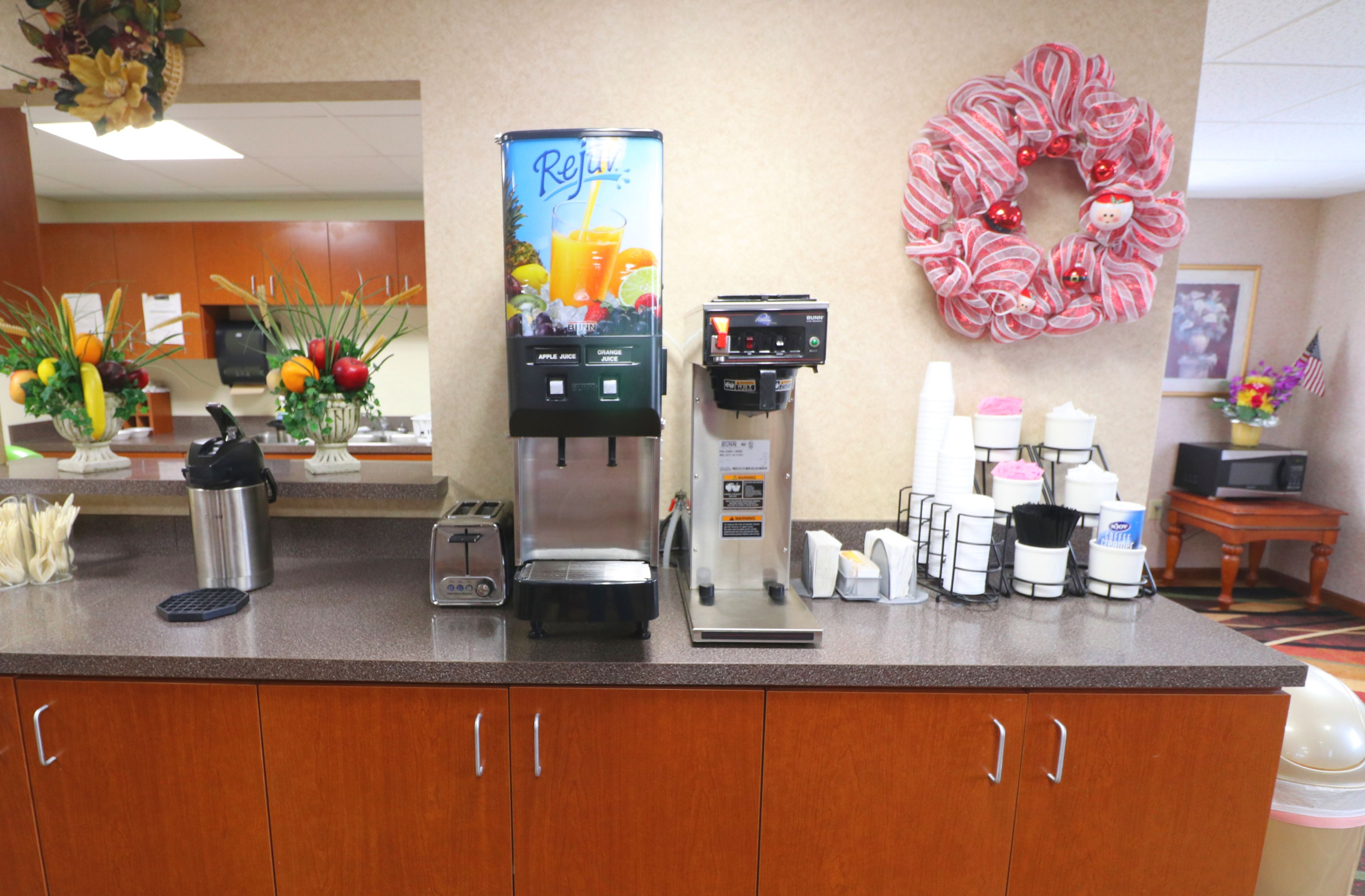 En hotellobby med en kaffemaskin, en juiceautomat och en dekorativ krans.