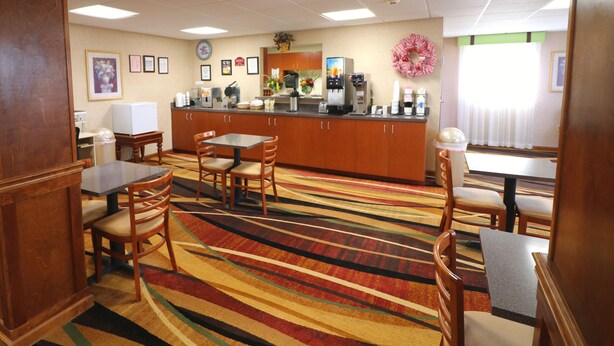 A hotel dining area with a kitchen in the background, featuring a colorful striped carpet, wooden furniture, and various kitchen appliances. - Jefferson Inn Dandridge (Dandridge)