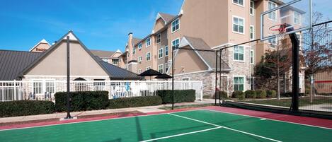 A tennis court with a net, surrounded by a fence, and buildings in the background.