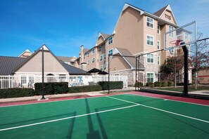 A tennis court with a net, surrounded by a fence, and buildings in the background.