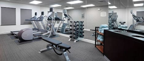 Un gimnasio con cintas de correr, elípticas, pesas libres y una banca.