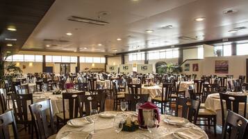 A large banquet hall with multiple round tables set for dining, each with white tablecloths and silverware.